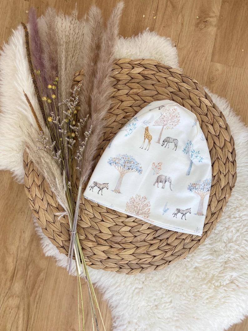 Wendemütze - Beanie für Kleinkinder aus Jersey in Weiß mit Tiermuster und Bäumen.