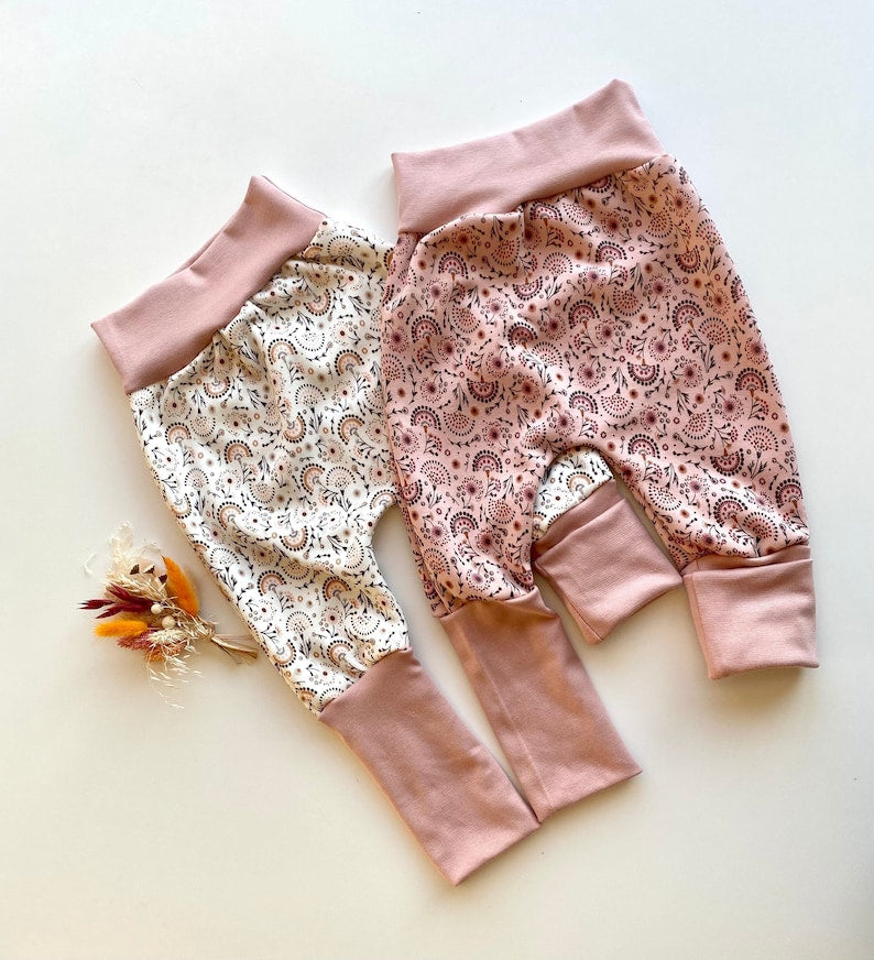 Zwei Pumphosen für Kleinkinder aus Alpenfleece in Weiß und Rosa mit Regenbogenmuster.