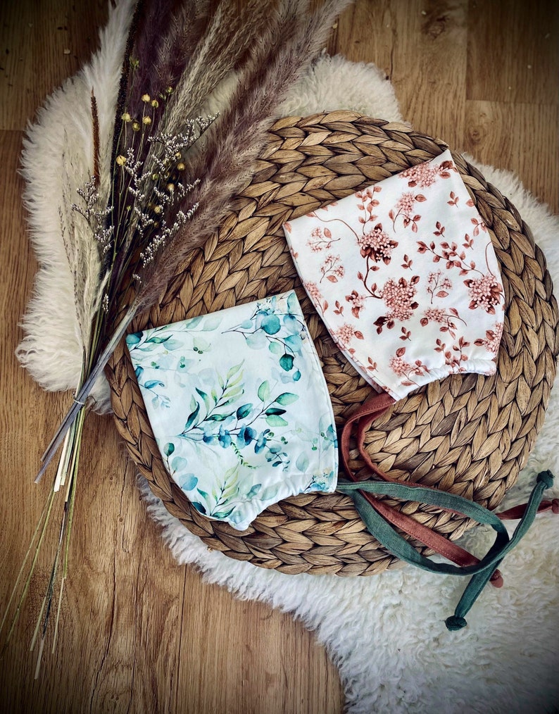 Zwei Zwergenmützen für Kleinkinder aus Jerseystoff in Weiß und hellem Türkis mit Blumenmuster.