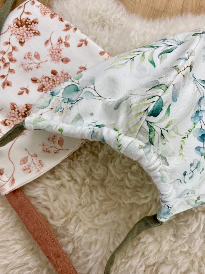 Zwei Zwergenmützen für Kleinkinder aus Jerseystoff in Weiß und Türkis mit Blumenmuster.